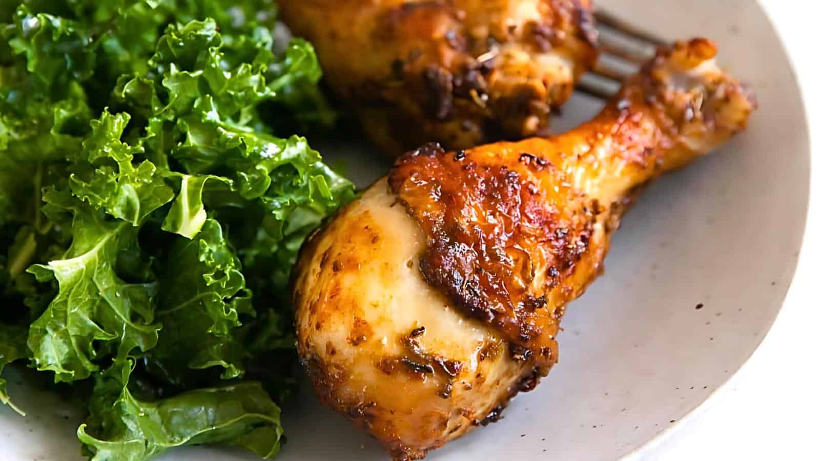 A plate with roasted chicken drumsticks and fresh kale.