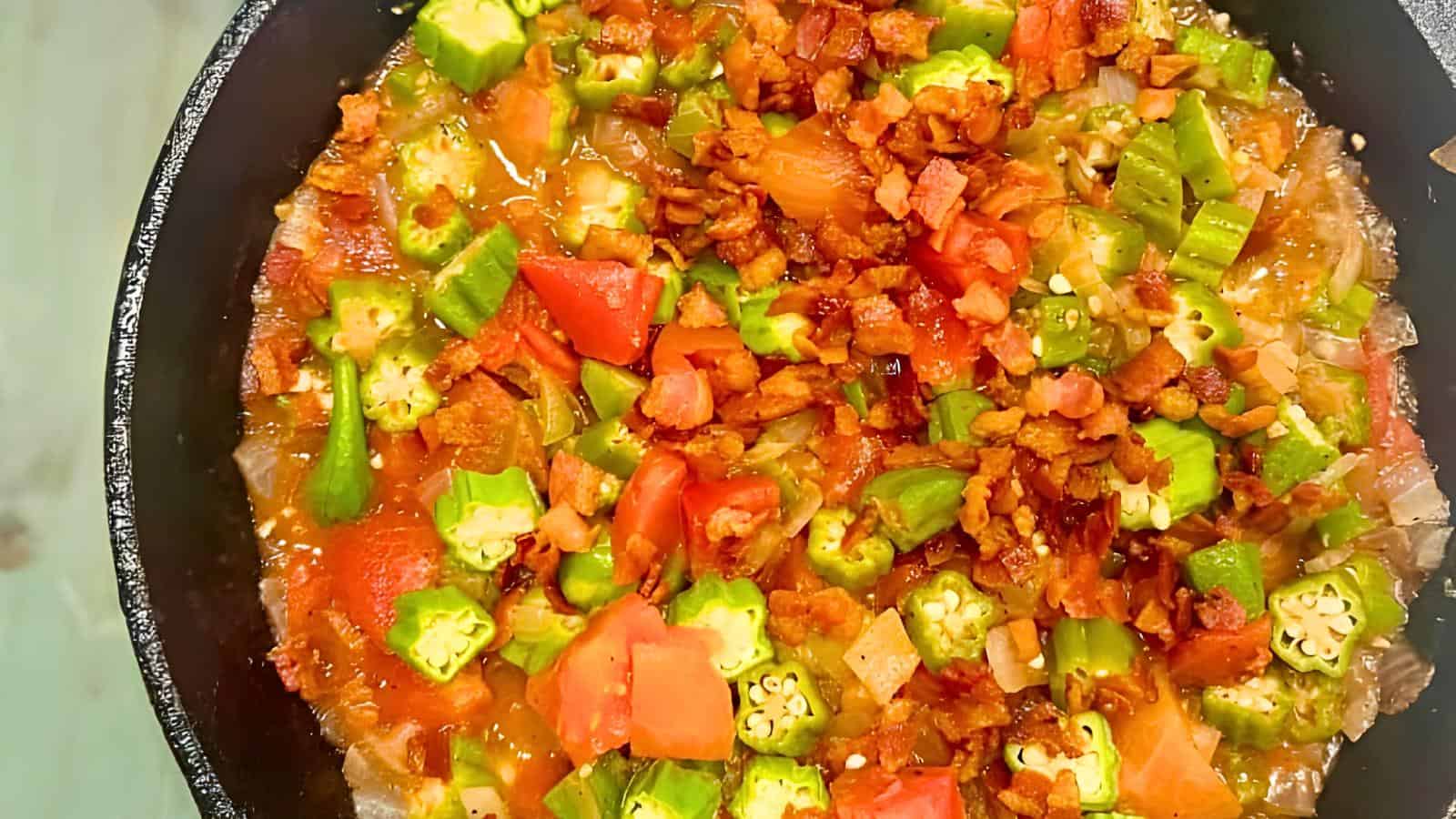 Chopped okra, tomatoes, and crumbled bacon in a skillet.