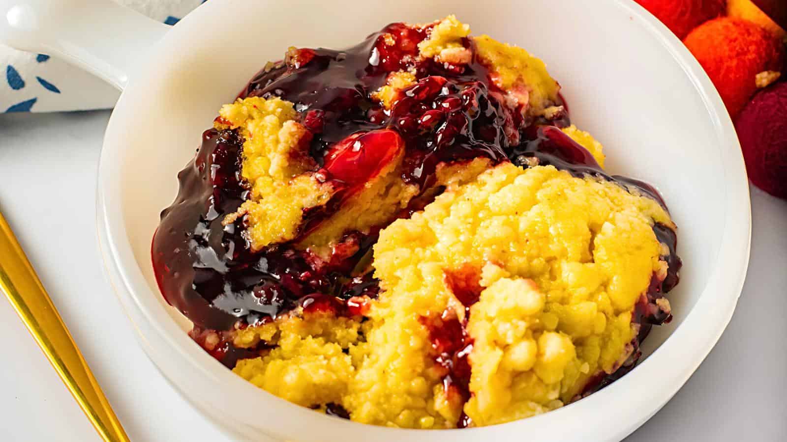 A white bowl with cobbler, topped with blackberry and strawberry compote.