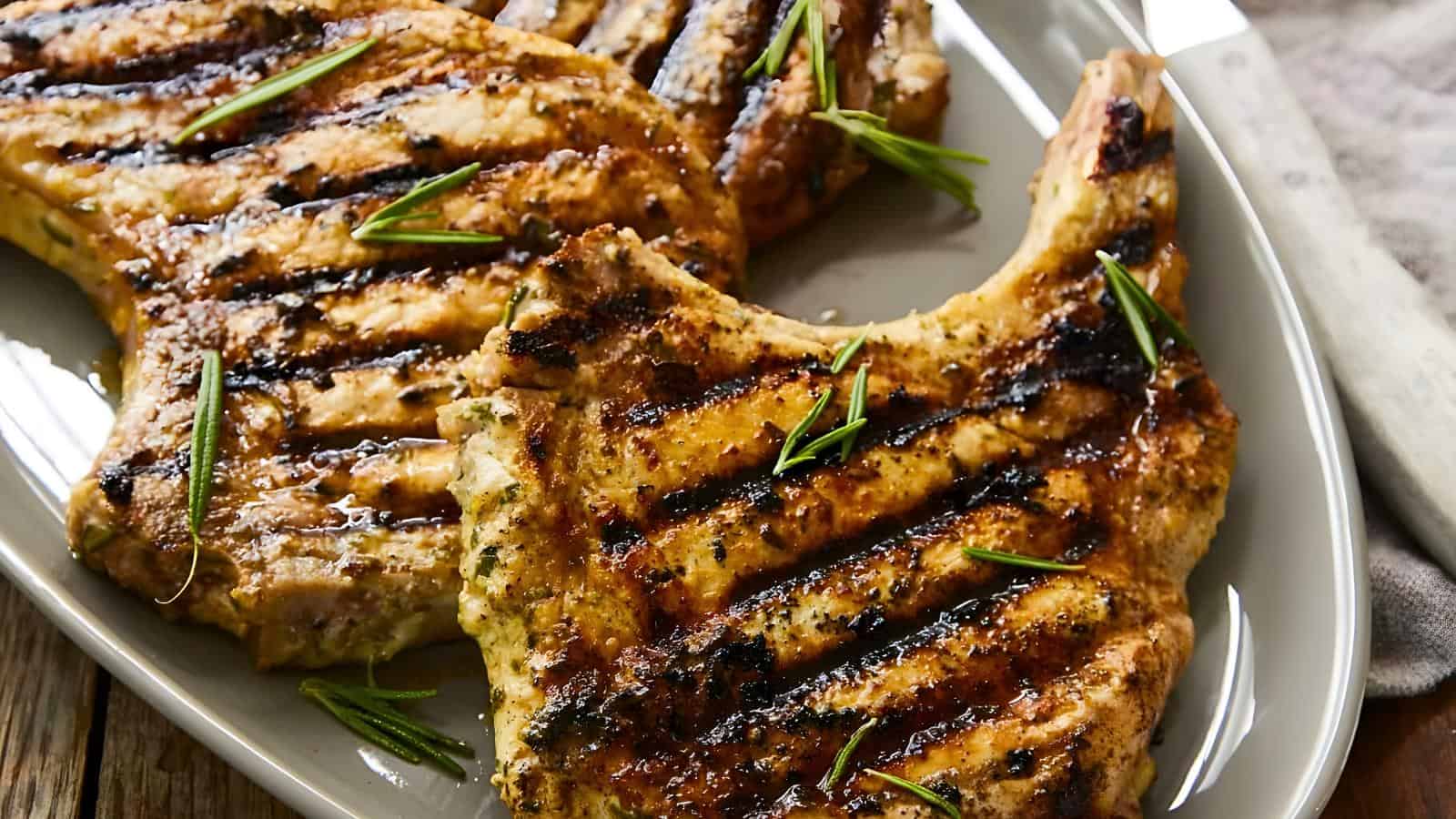 Grilled pork chops garnished with rosemary on a white plate.