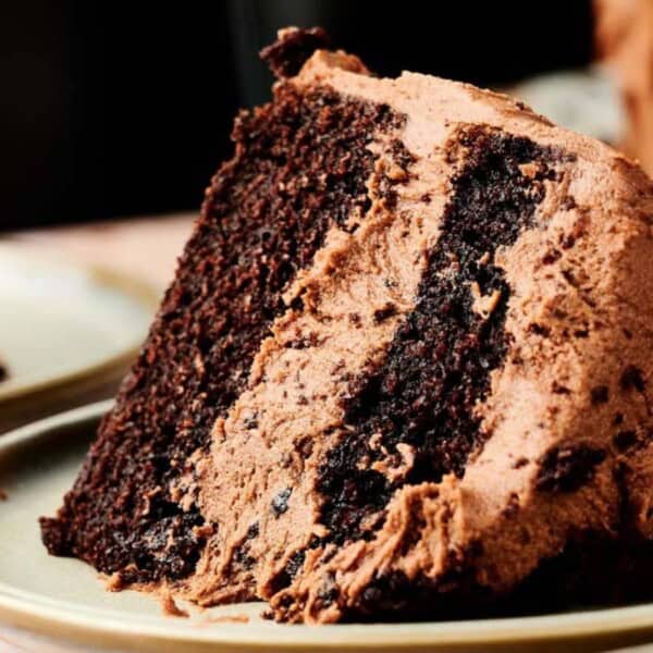 A close-up of a slice of chocolate cake with a layer of chocolate frosting and chocolate crumble, served on a light green plate.
