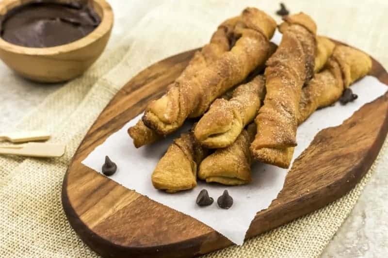 Air Fryer Churros on a wooden board with chocolate sauce in a bowl in the background.