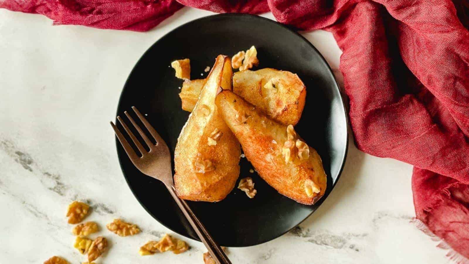 Air fryer pears sit on a black plate topped with walnuts.