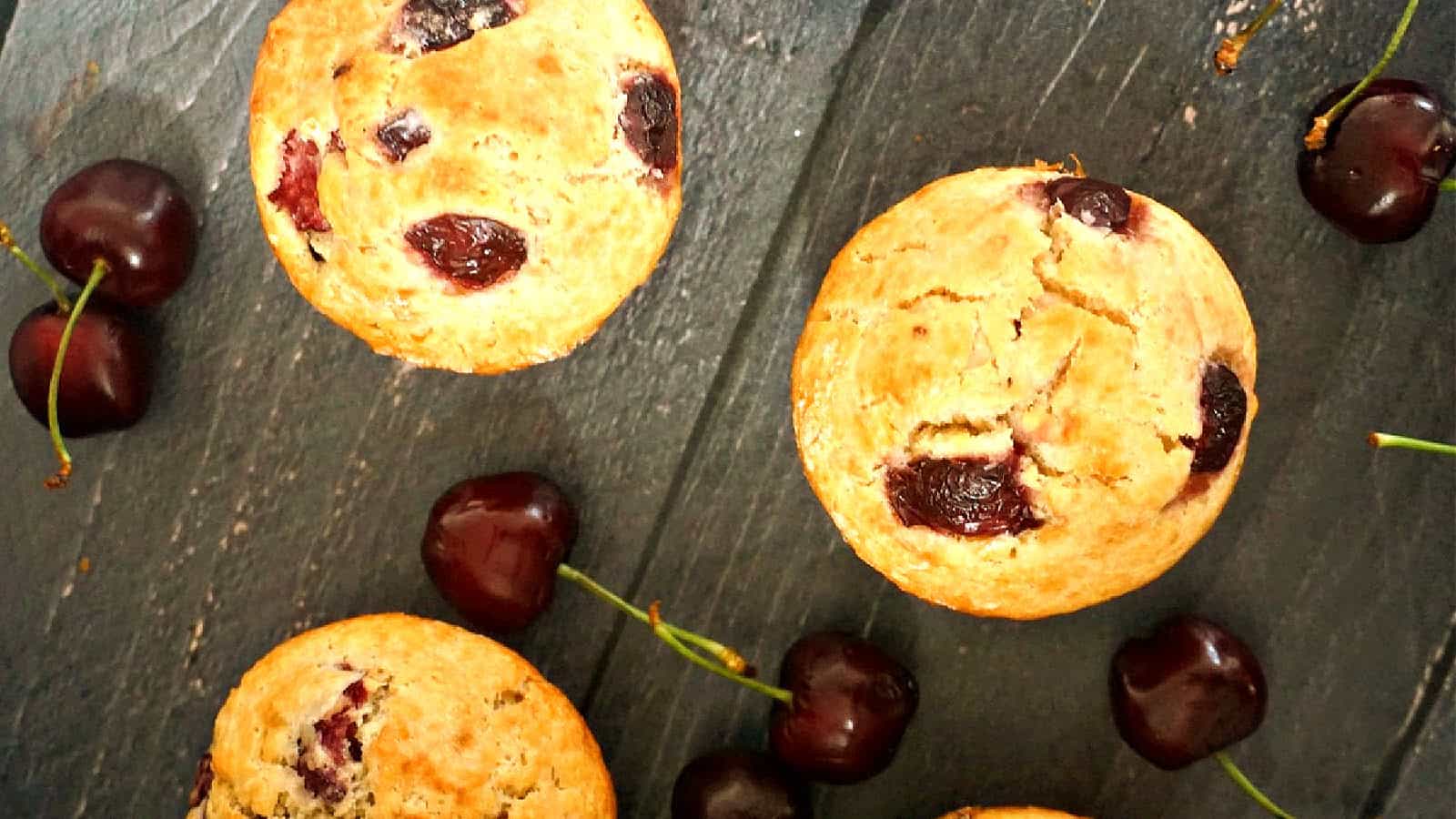 3 cherry muffins with fresh cherries around.