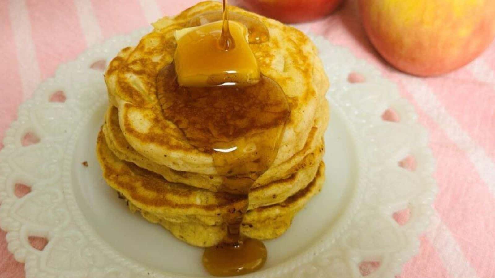 A white plate with a stack of pancakes with melting butter and syrup dripping.