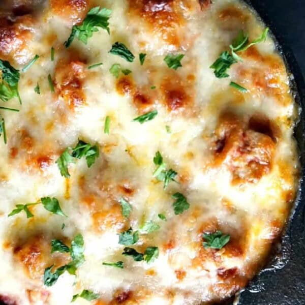 A skillet with meatball spaghetti bake and garnished with chopped parsley.