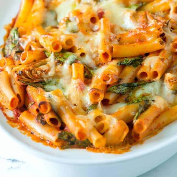 Baked ziti with green leaves in a white oval casserole dish.