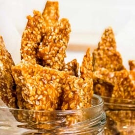 Glass jars filled with pieces of benne seed brittle on a white surface.