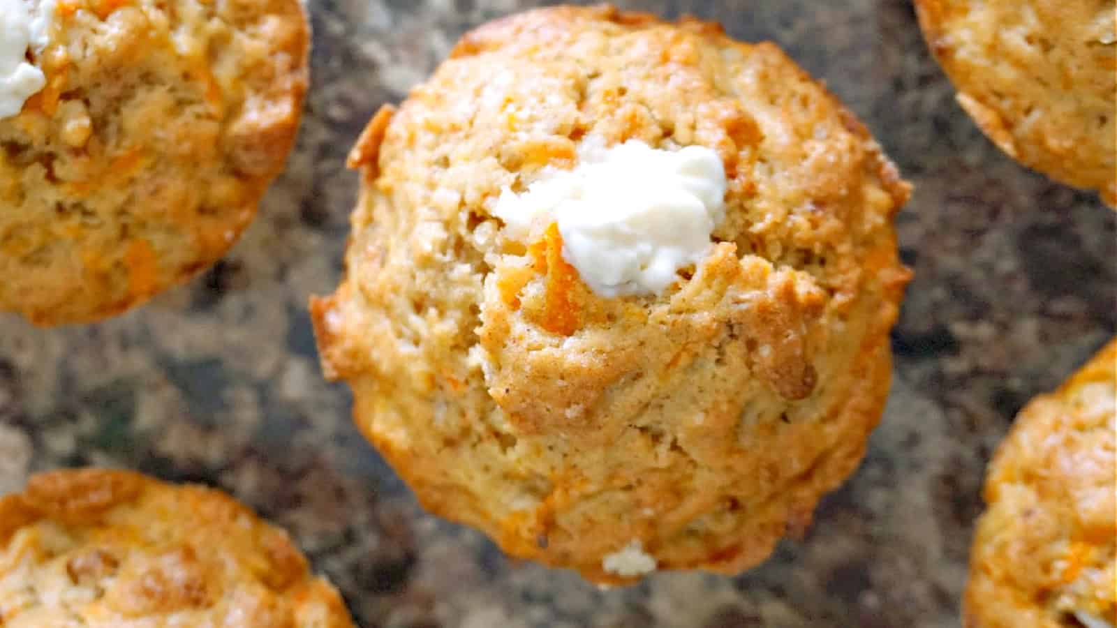 A carrot cake muffin with cream cheese topping with other muffins around.