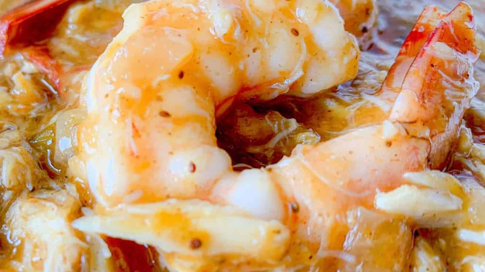 Close-up of a cooked shrimp in a rich, seasoned sauce. The shrimp is coated with the sauce, displaying a glossy appearance and pink hue.