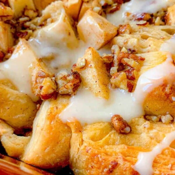 Close-up of baked cinnamon rolls topped with chopped pecans, apple chunks, and drizzled with white icing.