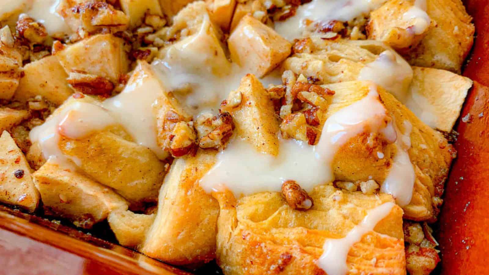 Close-up of baked cinnamon rolls topped with chopped pecans, apple chunks, and drizzled with white icing.