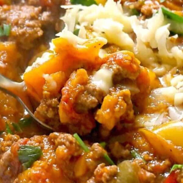 A bowl of lasagna soup with visible ground beef, noodles, tomato sauce, melted cheese, fresh herbs, and a fork scooping some up.