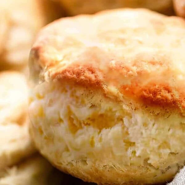 A close-up of a golden, flaky biscuit on a gray cloth, with several biscuits softly blurred in the background.