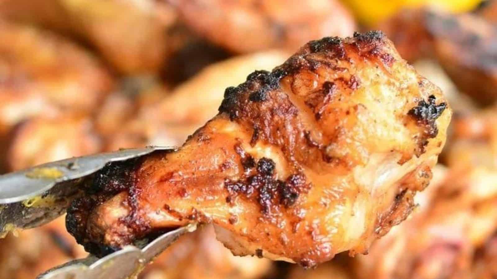 Metal tongs holding a charred and crispy grilled chicken drumstick.