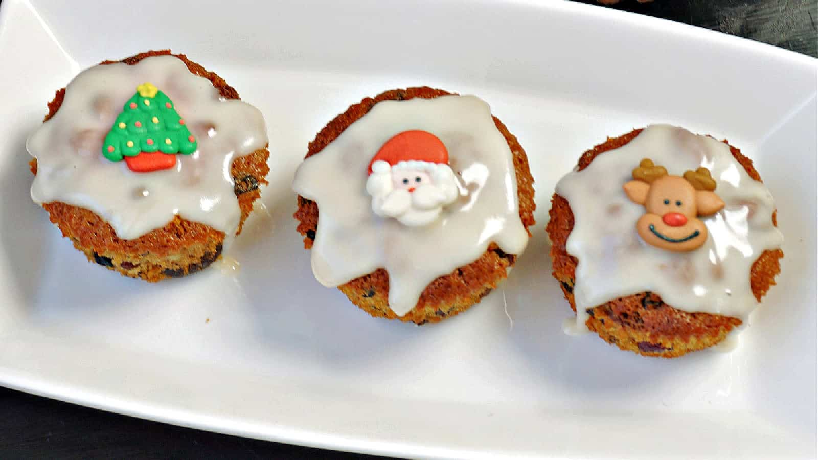 3 mini Christmas cakes on a white rectangle plate.