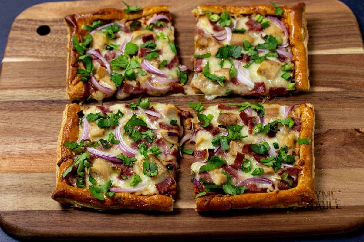 "Four square pizzas with onions and bacon on a wooden cutting board.	"