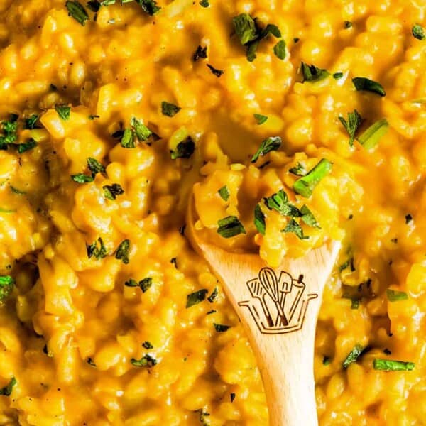 A pan filled with creamy yellow risotto, garnished with chopped herbs. A wooden spoon is placed in the center of the dish.
