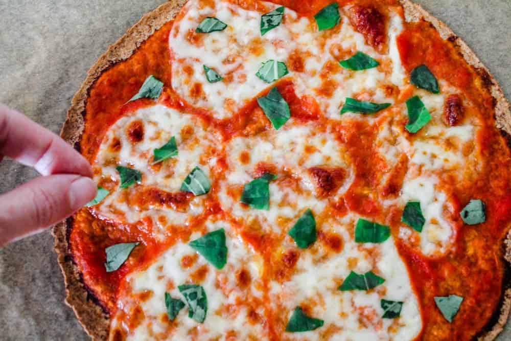 A hand sprinkling fresh basil on top of a tortilla pizza.