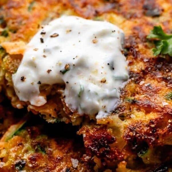Close-up of crispy vegetable fritters topped with a dollop of creamy sauce and garnished with fresh parsley.