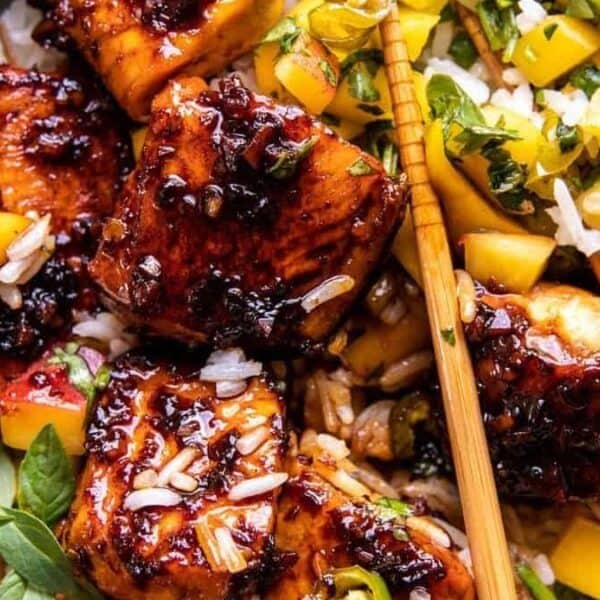Grilled glazed chicken pieces on white rice, topped with fresh herbs and accompanied by a colorful mango salsa; chopsticks placed to the side.
