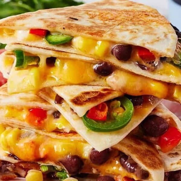 A stack of quesadilla wedges filled with melted cheese, black beans, corn, red pepper, and sliced jalapeños on a red plate with a side of sour cream.
