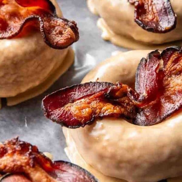 A close-up view of maple-glazed donuts topped with crispy bacon strips, arranged on a parchment-lined tray.