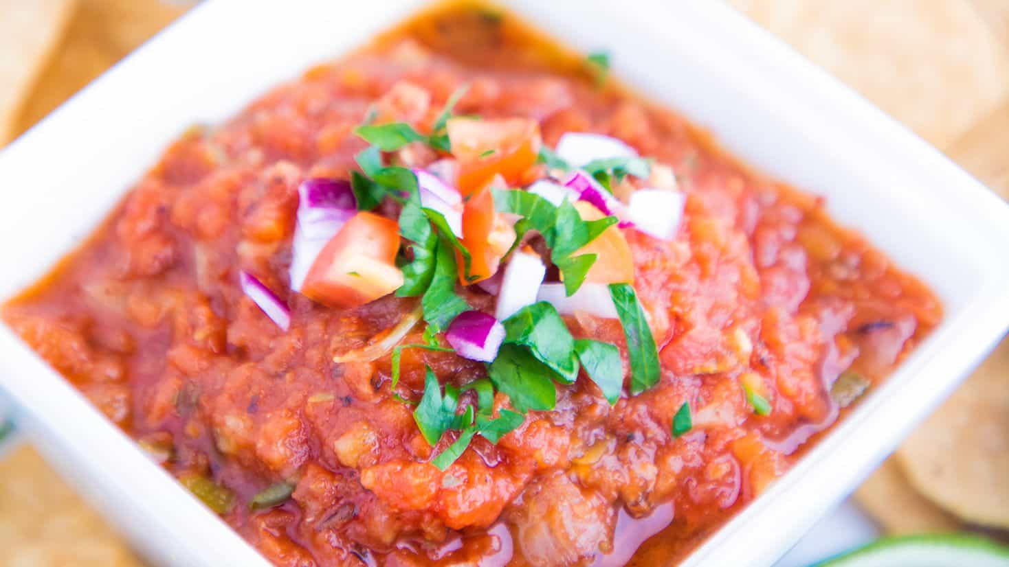 A bowl of salsa with diced tomatoes, onions, and cilantro garnished on top.
