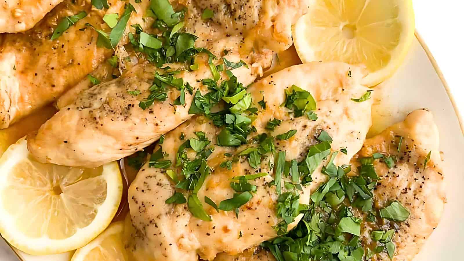 A plate of lemon herb chicken garnished with fresh parsley and slices of lemon. The chicken breasts appear juicy and seasoned, with the herbs and lemon slices adding a vibrant touch to the dish.