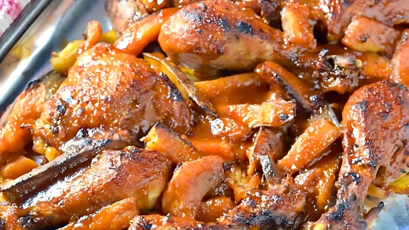 A close-up of a savory dish featuring succulent pieces of grilled or roasted meat, generously coated in a rich, reddish-brown sauce. The meat appears crispy on the edges, with visible herbs and spices. The sauce glistens, enhancing the dish's appetizing appearance.