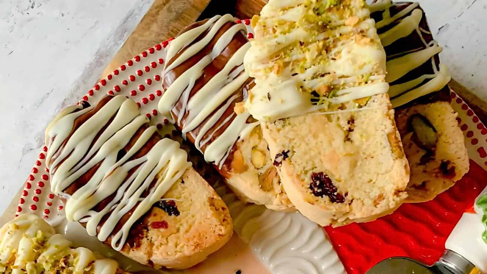 A plate of biscotti cookies, some drizzled with white chocolate and others with dark chocolate, garnished with nuts and dried fruits.