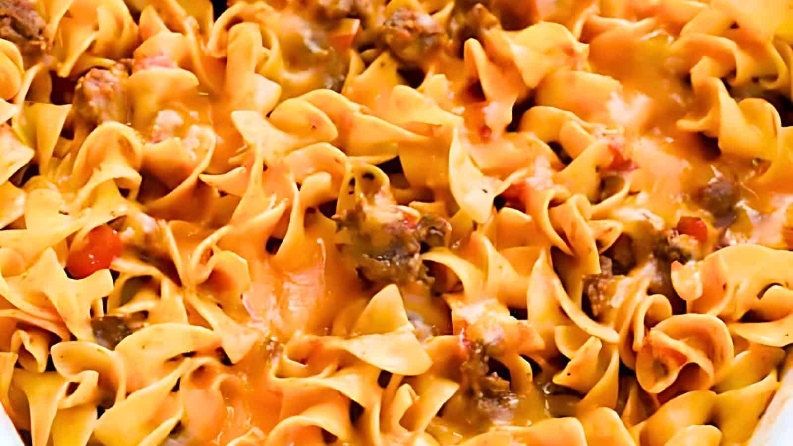 A close-up image of a baked pasta casserole, featuring wide, ribbon-like egg noodles mixed with ground beef and covered in melted cheese. The dish appears hearty and comforting with a golden-brown finish.