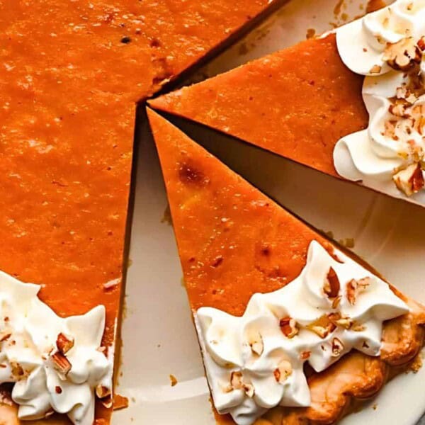 A pumpkin pie with two partially removed slices, garnished with whipped cream and chopped nuts.