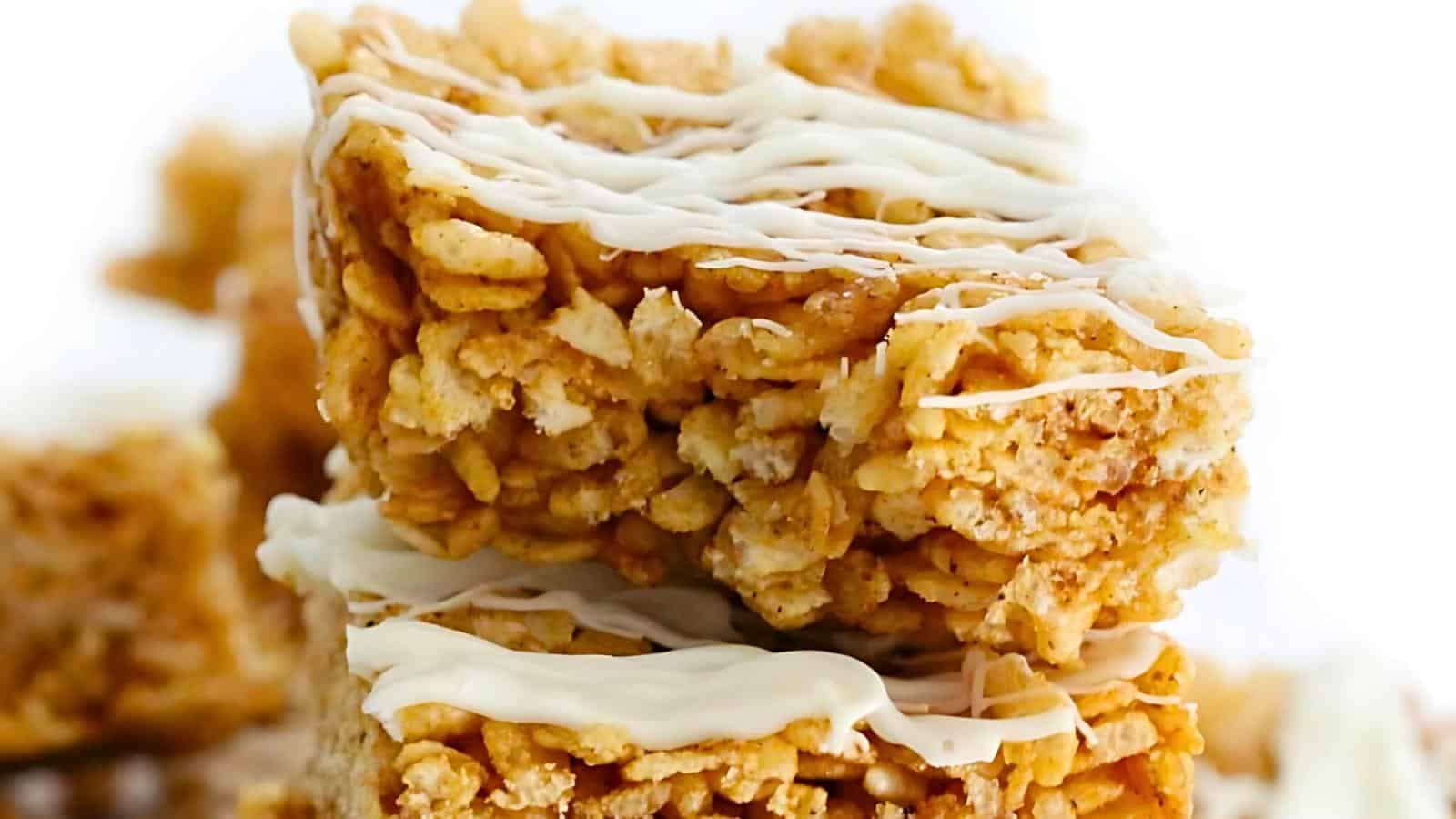 Close-up of two stacked rice cereal treats drizzled with white chocolate. The treats are golden-brown with a crispy texture and have a light coating of white chocolate lines on top.