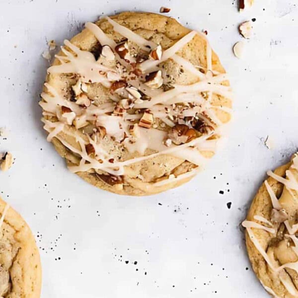 Five cookies topped with chopped nuts and drizzled icing on a white surface.