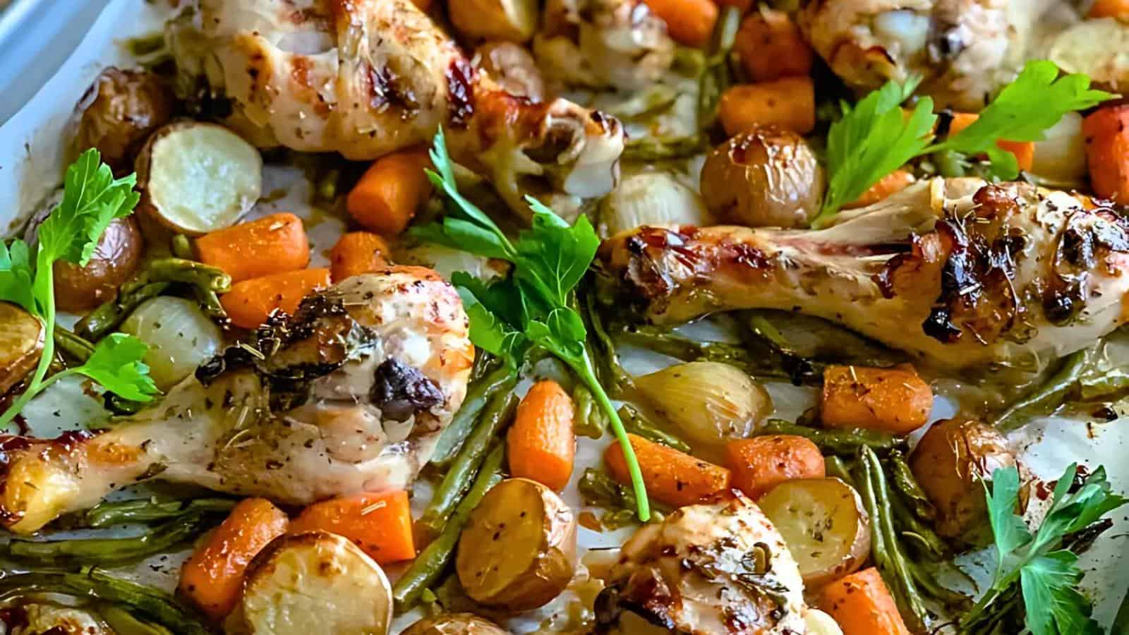 A tray of roasted chicken drumsticks, carrots, green beans, and baby potatoes, garnished with fresh parsley. The chicken is golden and slightly charred, and the vegetables are evenly roasted to a tender texture.