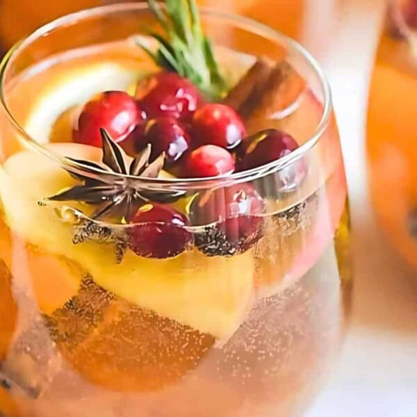 A glass of punch with lemon slices, cranberries, a cinnamon stick, star anise, and a rosemary sprig as garnish.