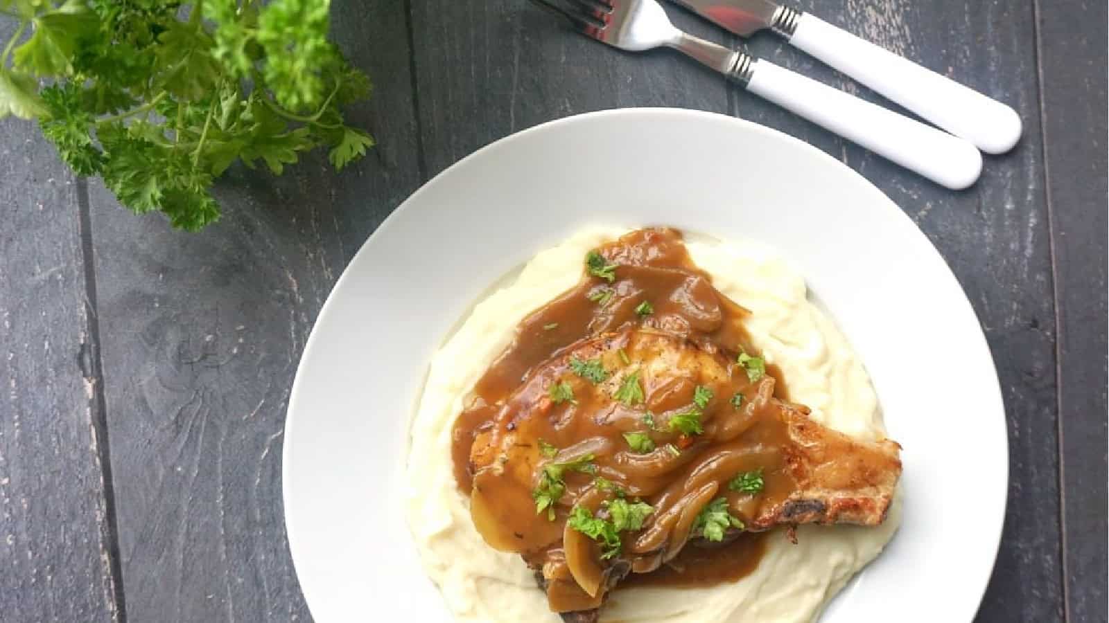 A pork chops in onion gravy over a bed of mash.