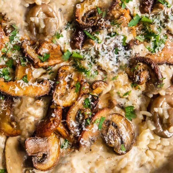 A close-up view of creamy mushroom risotto in a pan. The dish features a rich mix of risotto rice, tender sautéed mushrooms, grated cheese, and fresh chopped parsley, creating a comforting and savory meal.