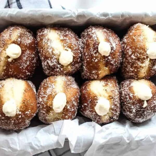 Eight sugar-coated, cream-filled doughnuts are arranged in a parchment-lined tray.