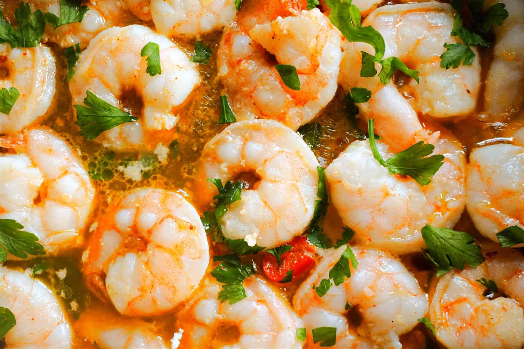 Cooked shrimp garnished with fresh parsley in a zesty sauce.