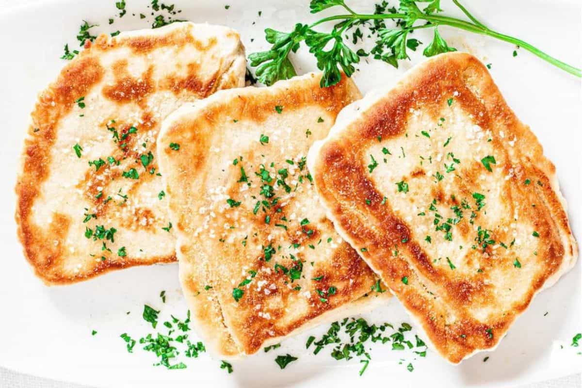 Three pieces of golden-brown grilled cheese bread, garnished with finely chopped parsley, are served on a white plate with a sprig of fresh parsley on the side.