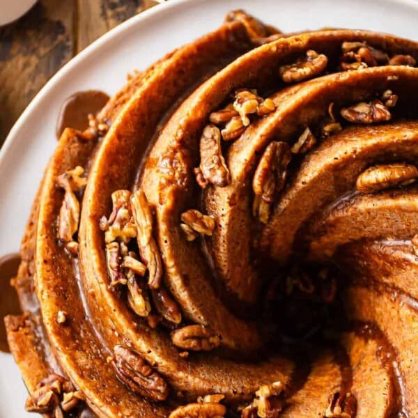 A swirl-shaped Bundt cake topped with pecans on a white plate with decorative trim, placed on a wooden surface.