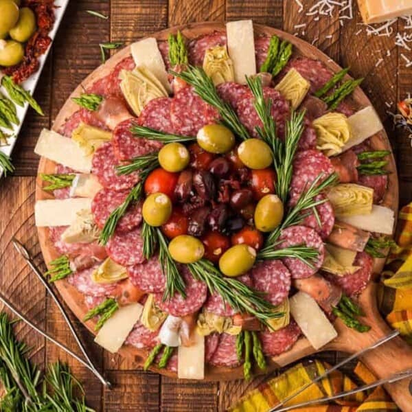 Salami, cheese, olives, artichokes, tomatoes, fresh rosemary, and assorted vegetables arranged on a wooden charcuterie board.
