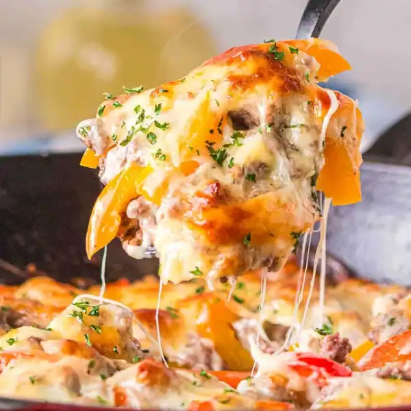 A portion of ground beef and bell pepper casserole with melted cheese is being lifted from a skillet, cheese stretching upwards.