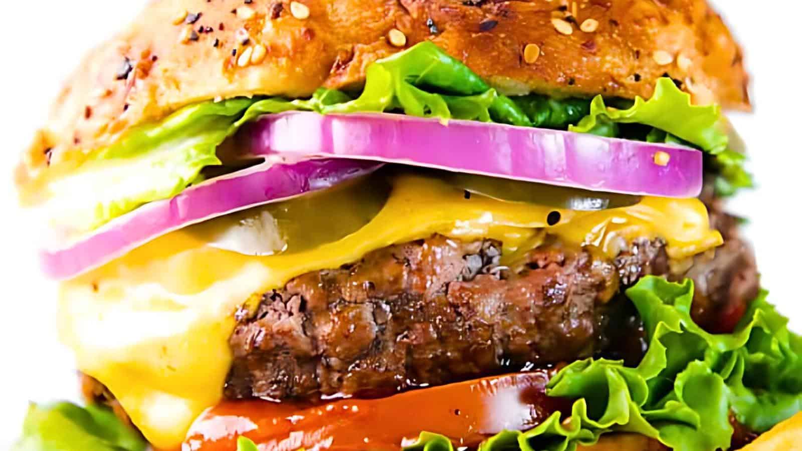 A close-up of a juicy cheeseburger with a sesame seed bun. The burger features layers of melted cheese, a beef patty, red onion rings, pickles, fresh green lettuce, tomato slices, and ketchup. The ingredients are stacked enticingly, showcasing a delicious presentation.
