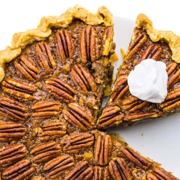 A southern pecan pie with a slice removed, topped with whipped cream, featuring a golden crust and whole pecans neatly arranged on the surface.