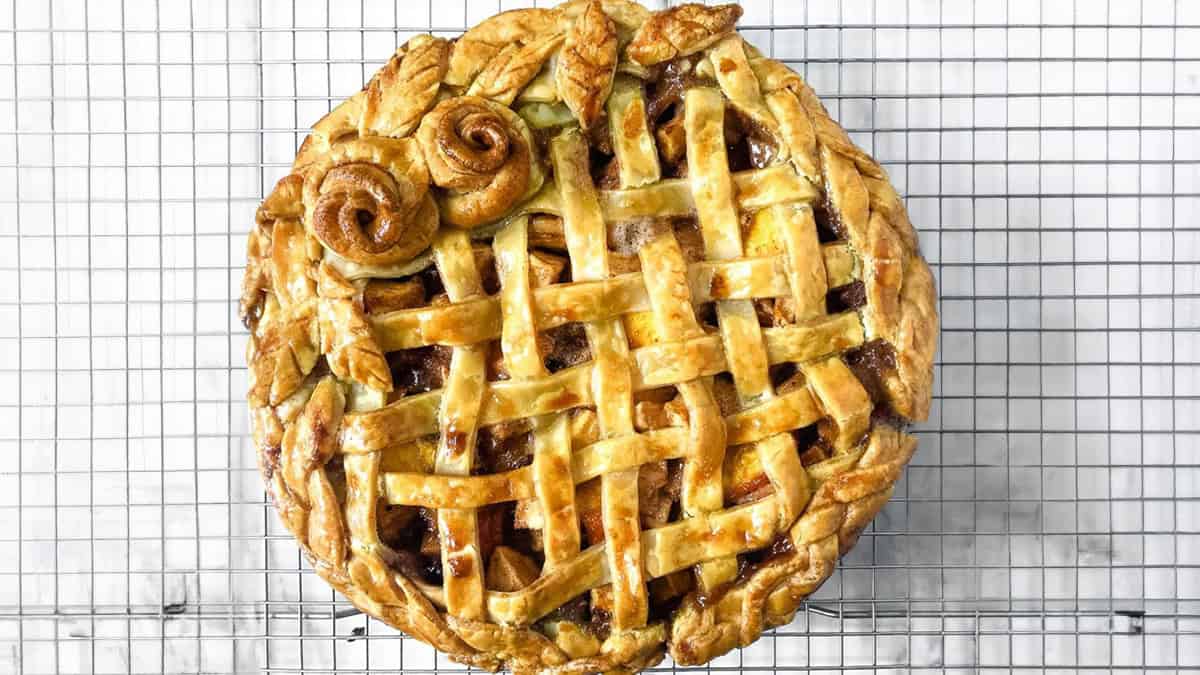 A lattice-topped pie with decorative flower-shaped pastries rests on a wire cooling rack.
