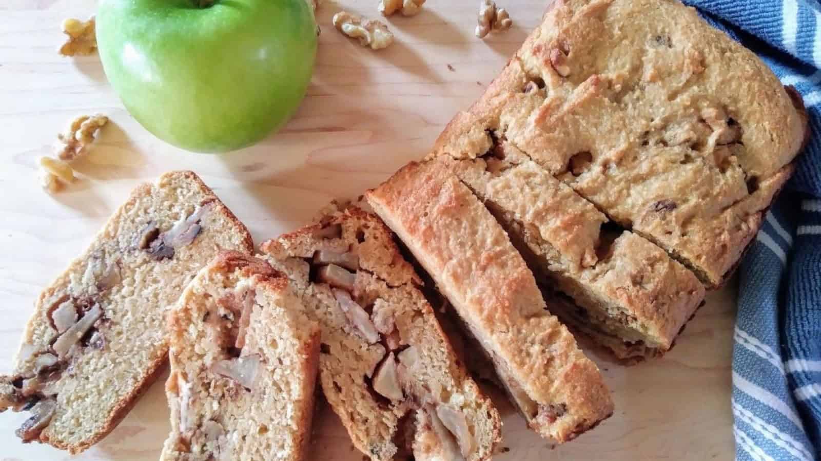slices of bread with chopped apples and walnut in the middle and a green apple on a wooden chopping board.