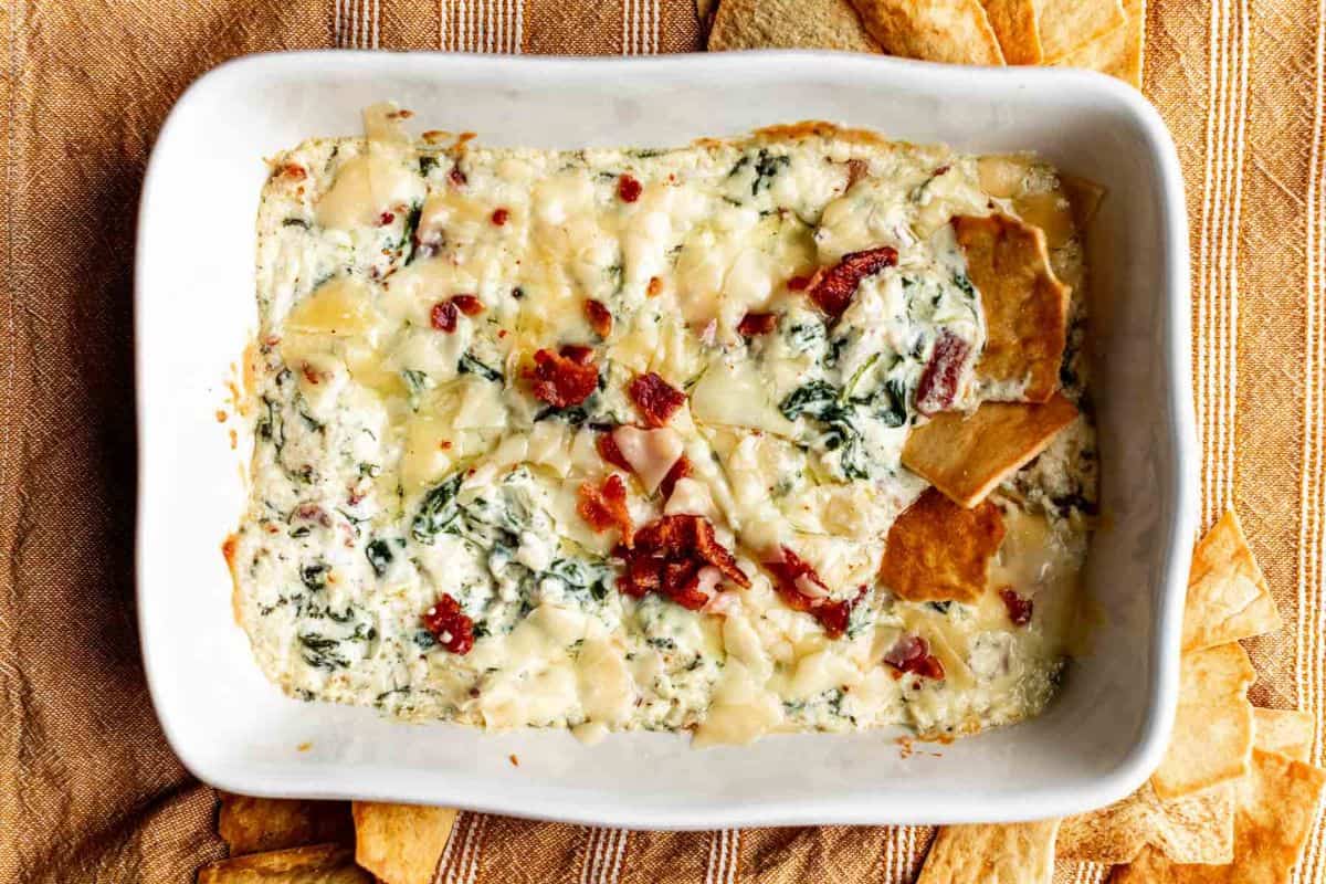 A baking dish of spinach and bacon dip with pita chips.